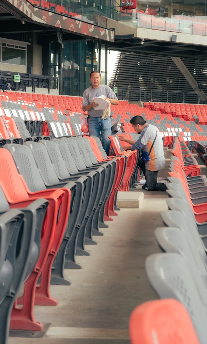 Two workers cleaning empty stadium seats, ensuring cleanliness before events.